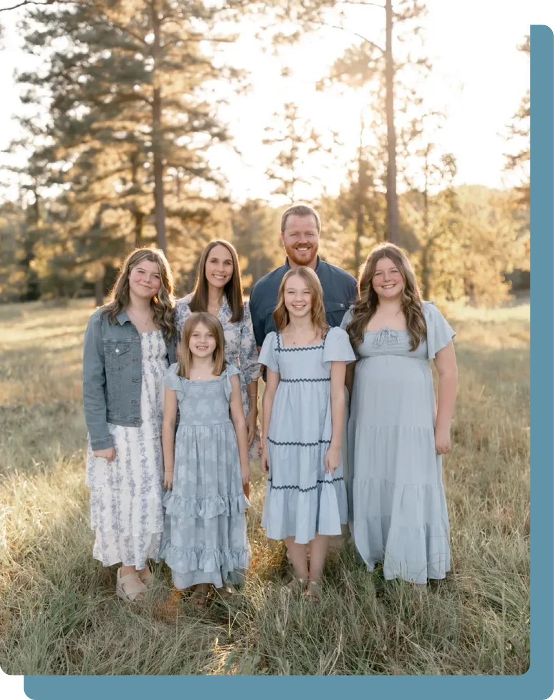 Family posing in sunny, wooded field.