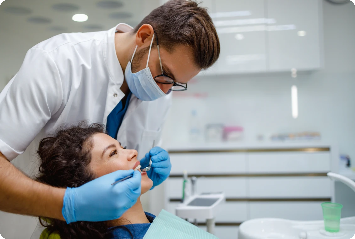 Dentist examining a patient's teeth, smiling.